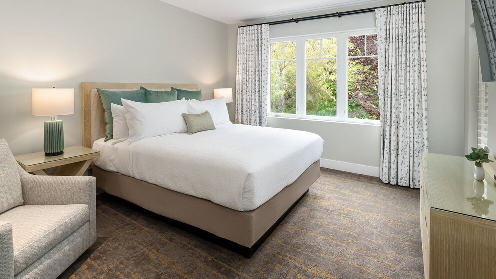 a bed with white sheets and pillows in a room with windows